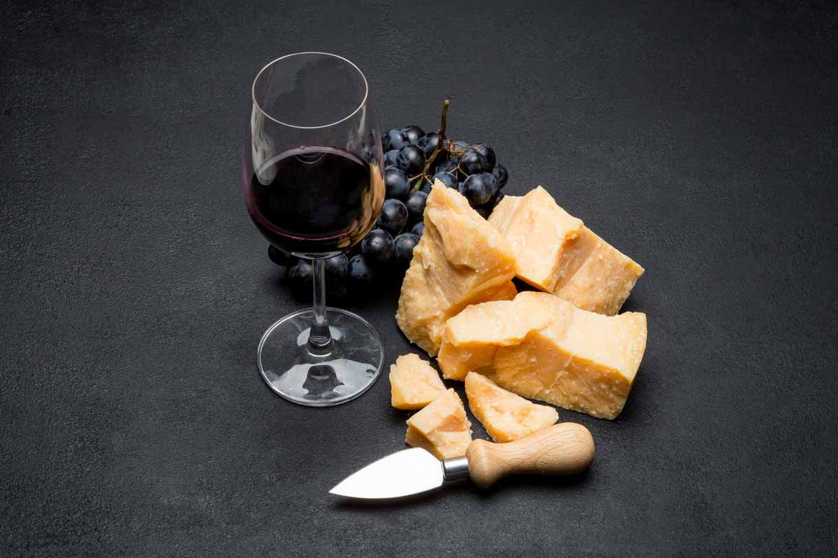 Scaglie di Parmigiano Reggiano abbinamento con bicchiere di vino rosso e uva - Gustoemilia